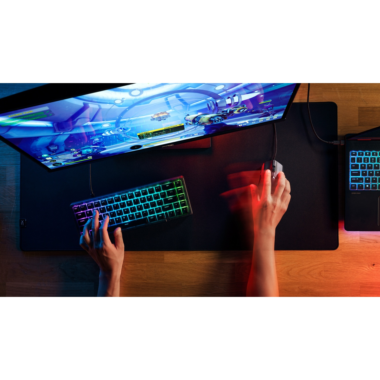 Vue de dessus d'un équipement de jeu avec moniteur, clavier RVB, souris en mouvement et ordinateur portable sur bureau.