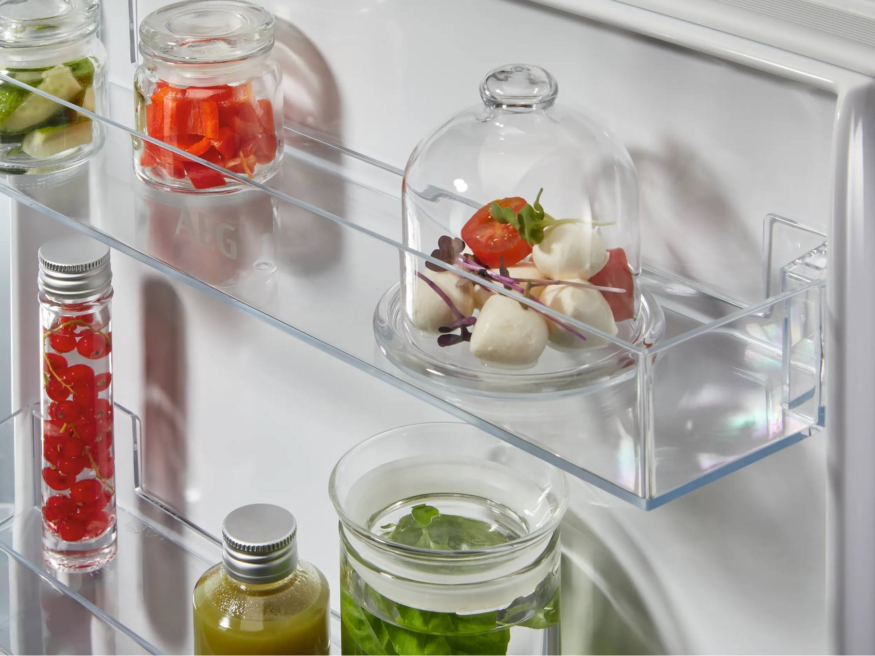 Recipientes de vidrio con comida como mozzarella, hierbas y frutos rojos dentro del refrigerador.