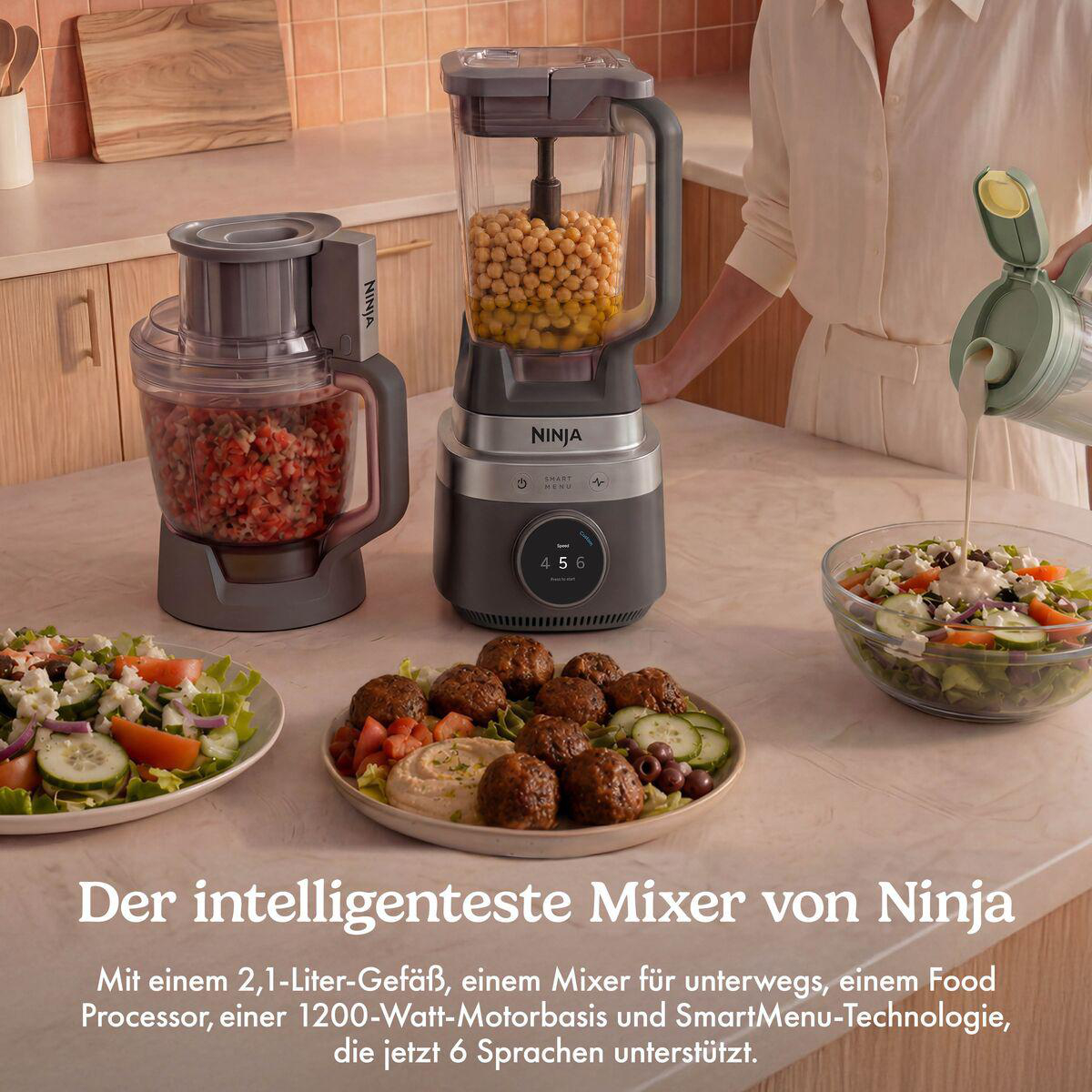 Ninja Mixer und Food Processor auf einer Küchentheke mit Salaten und Fleischbällchen.