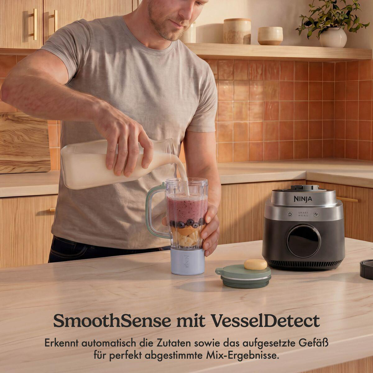 Ein Mann gießt Milch in einen Ninja-Mixer mit Früchten auf einer Holzarbeitsplatte in einer Küche.