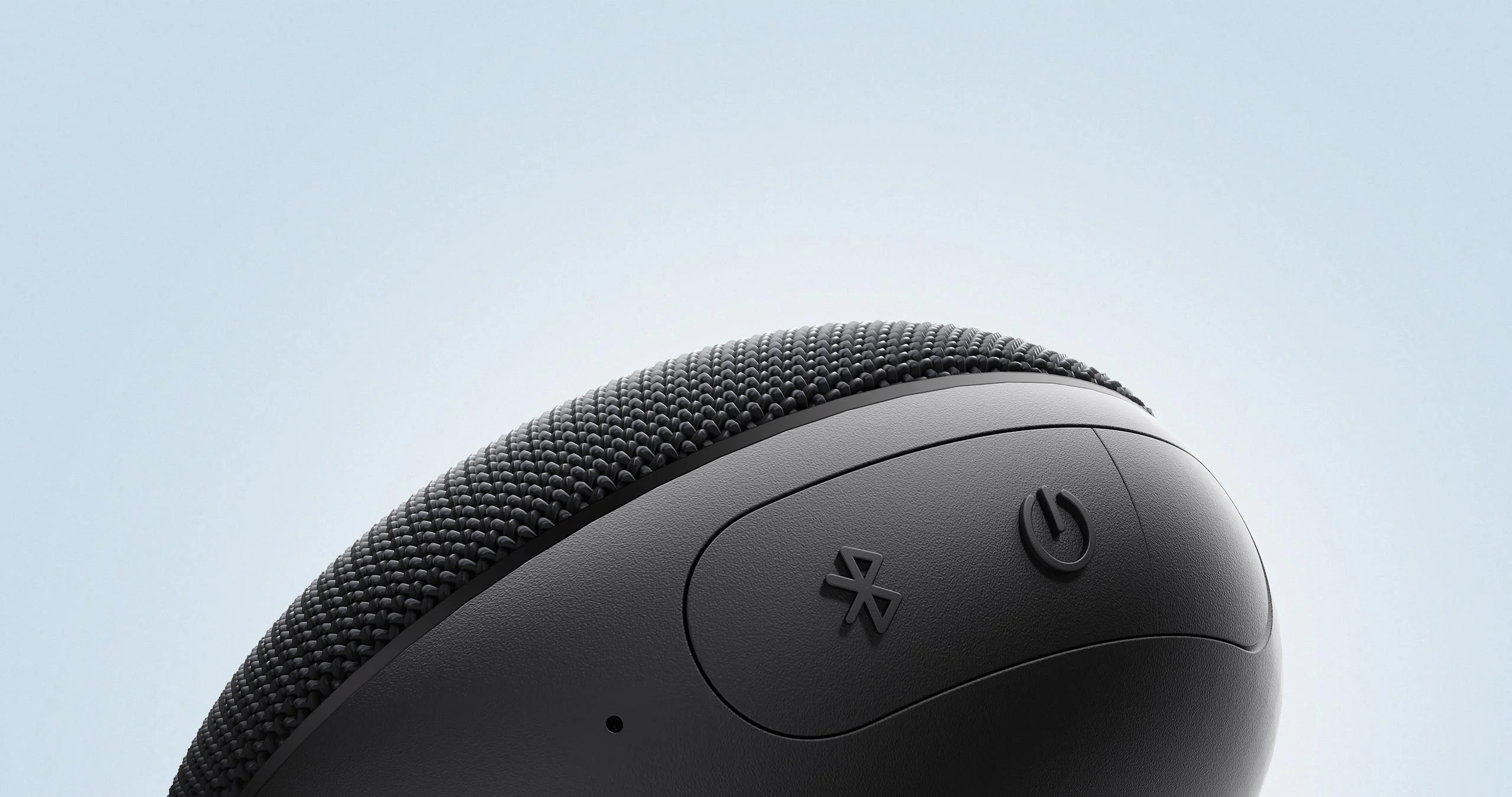 Fekete, kerek hangszóró Bluetooth- és bekapcsológombokkal, világos háttér előtt.