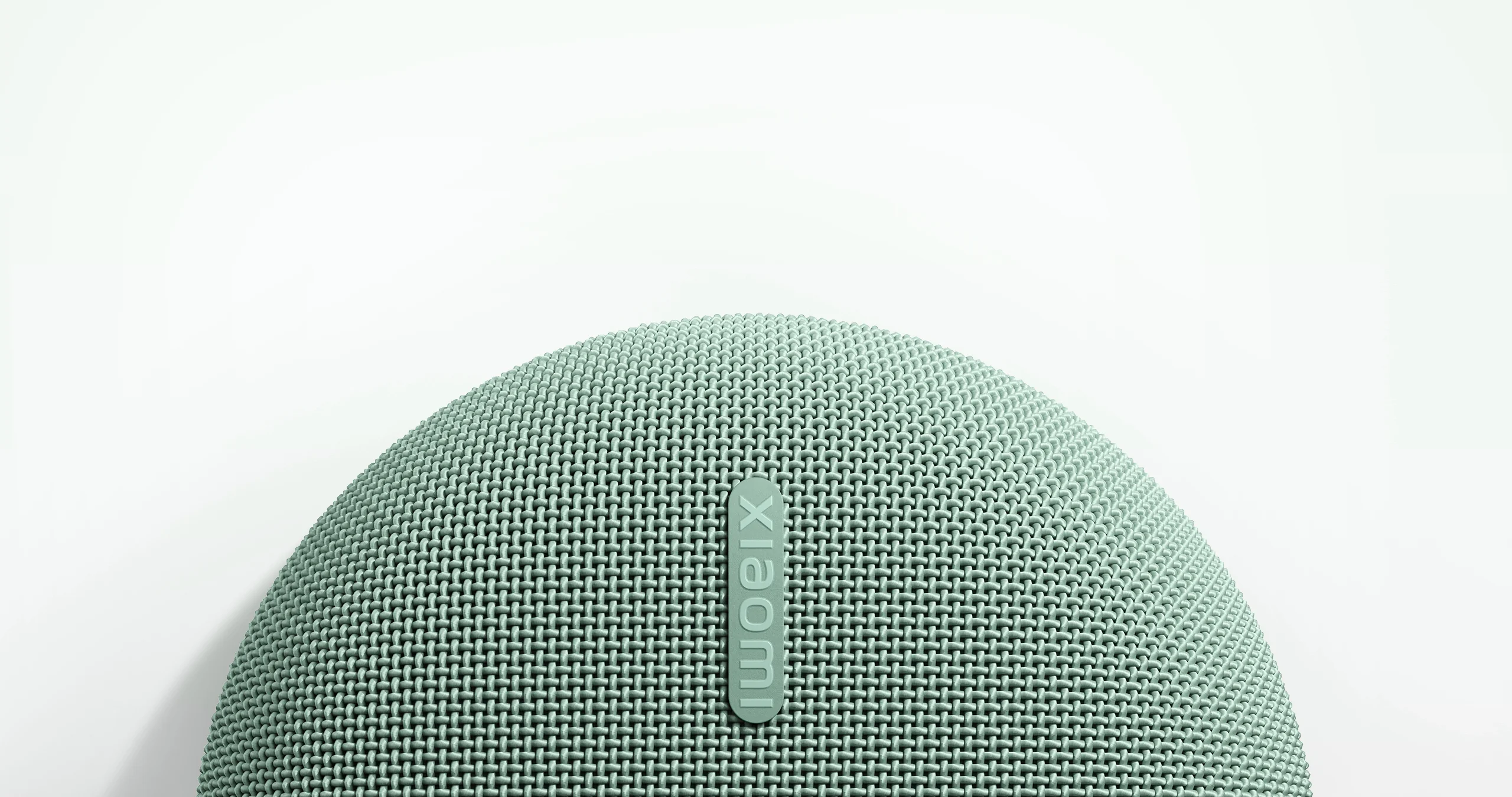 Világoszöld, szövetborítású Xiaomi hangszóró fehér háttér előtt.