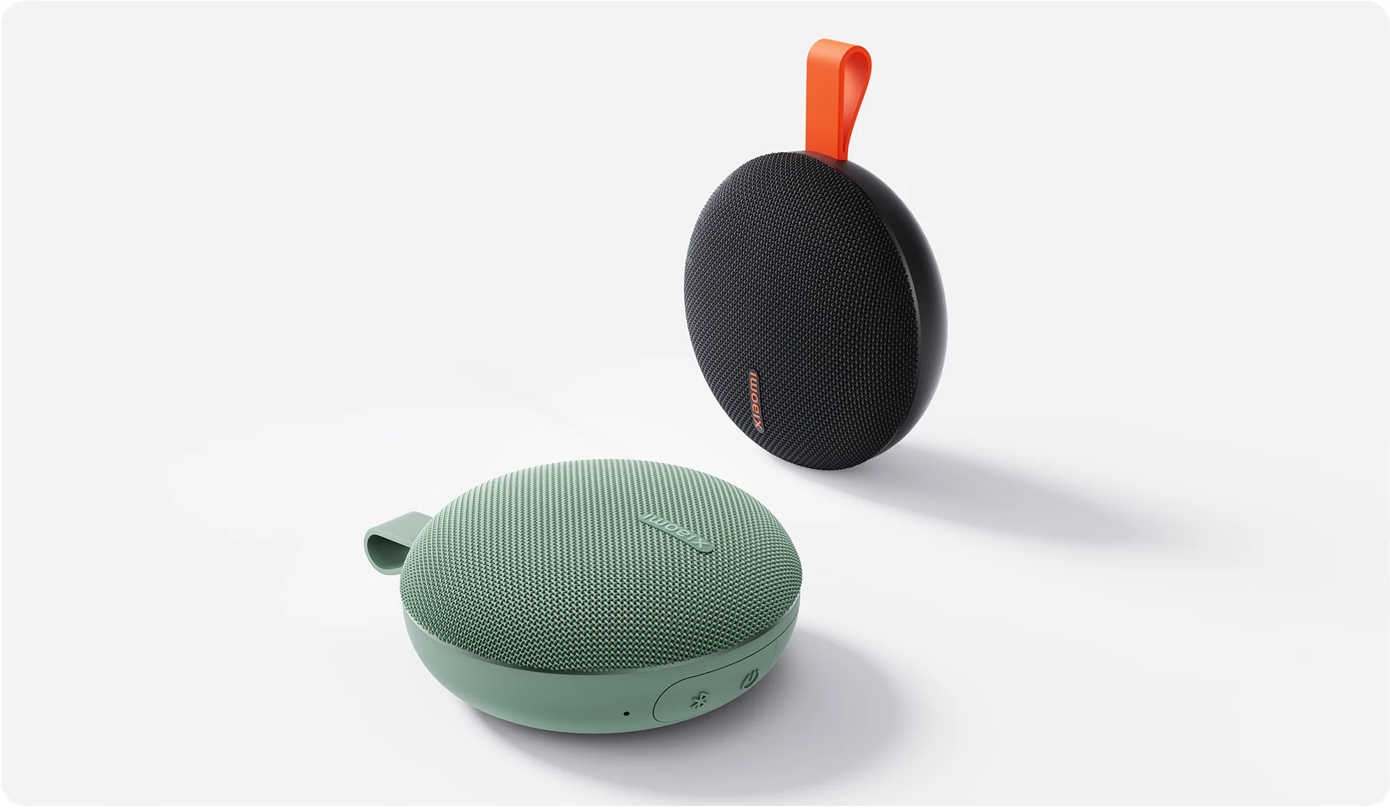 Két kerek Xiaomi Bluetooth hangszóró fehér alapon: az egyik mentazöld, a másik fekete narancssárga pánttal.