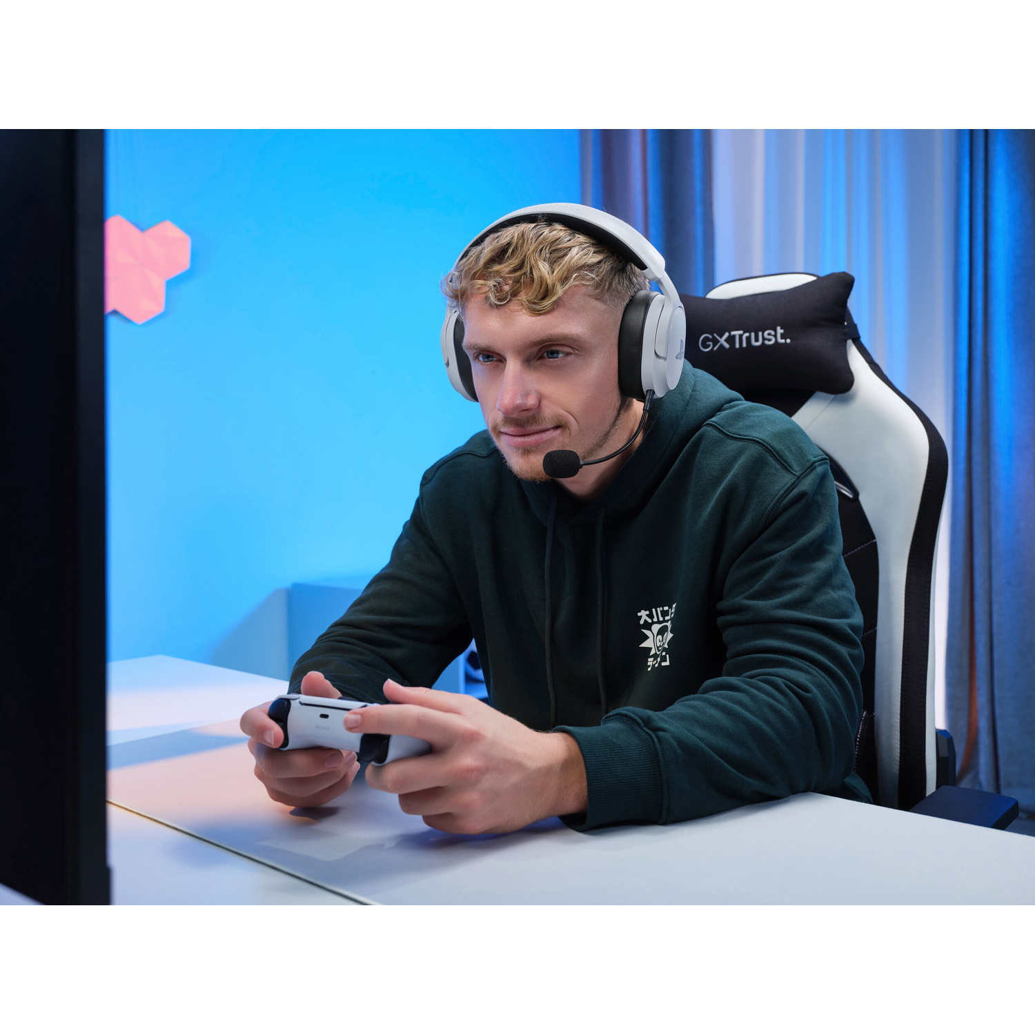 Un giovane con cuffie e felpa verde siede a una scrivania giocando ai videogiochi con un controller.