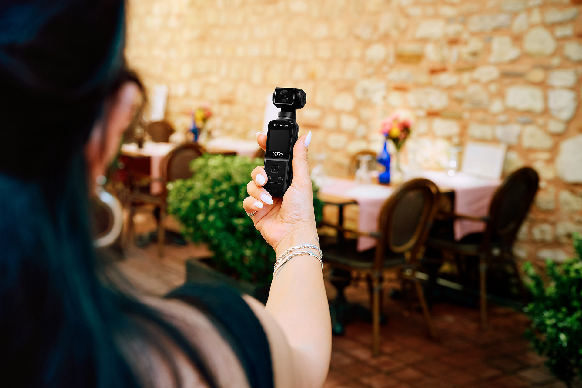 Bir kadın, bir restoran terasının önünde küçük siyah bir 4K cep kamerası tutuyor.