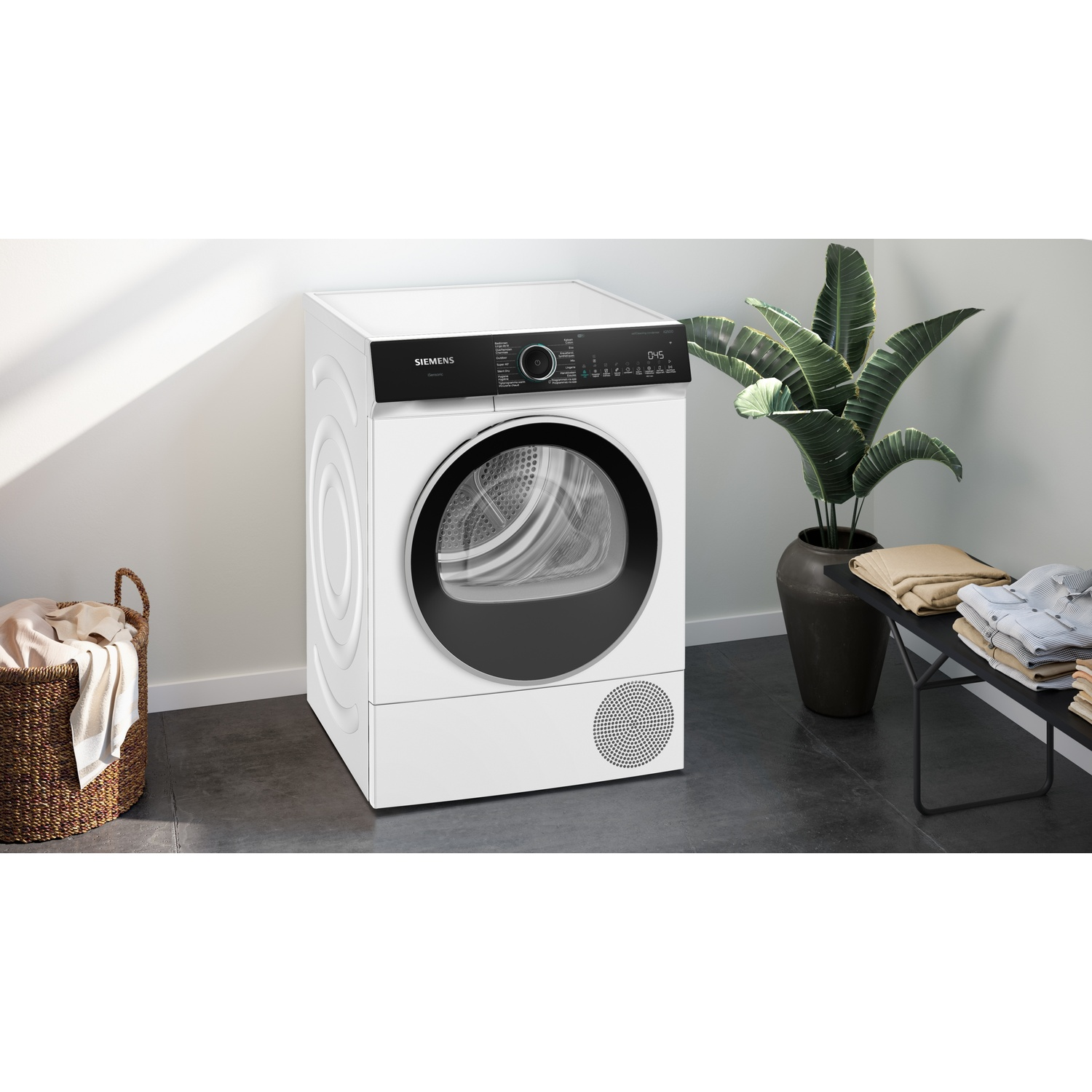 Een witte Siemens wasdroger in een moderne kamer met een plant en wasgoed.