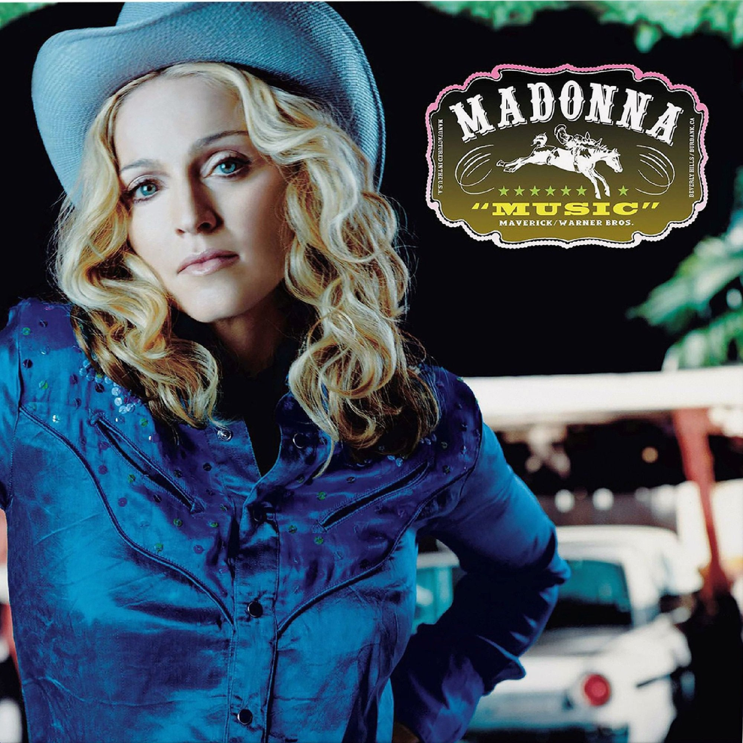 Madonna draagt een cowboyhoed en blauw hemd voor een auto, met het Music-albumlogo rechtsboven.