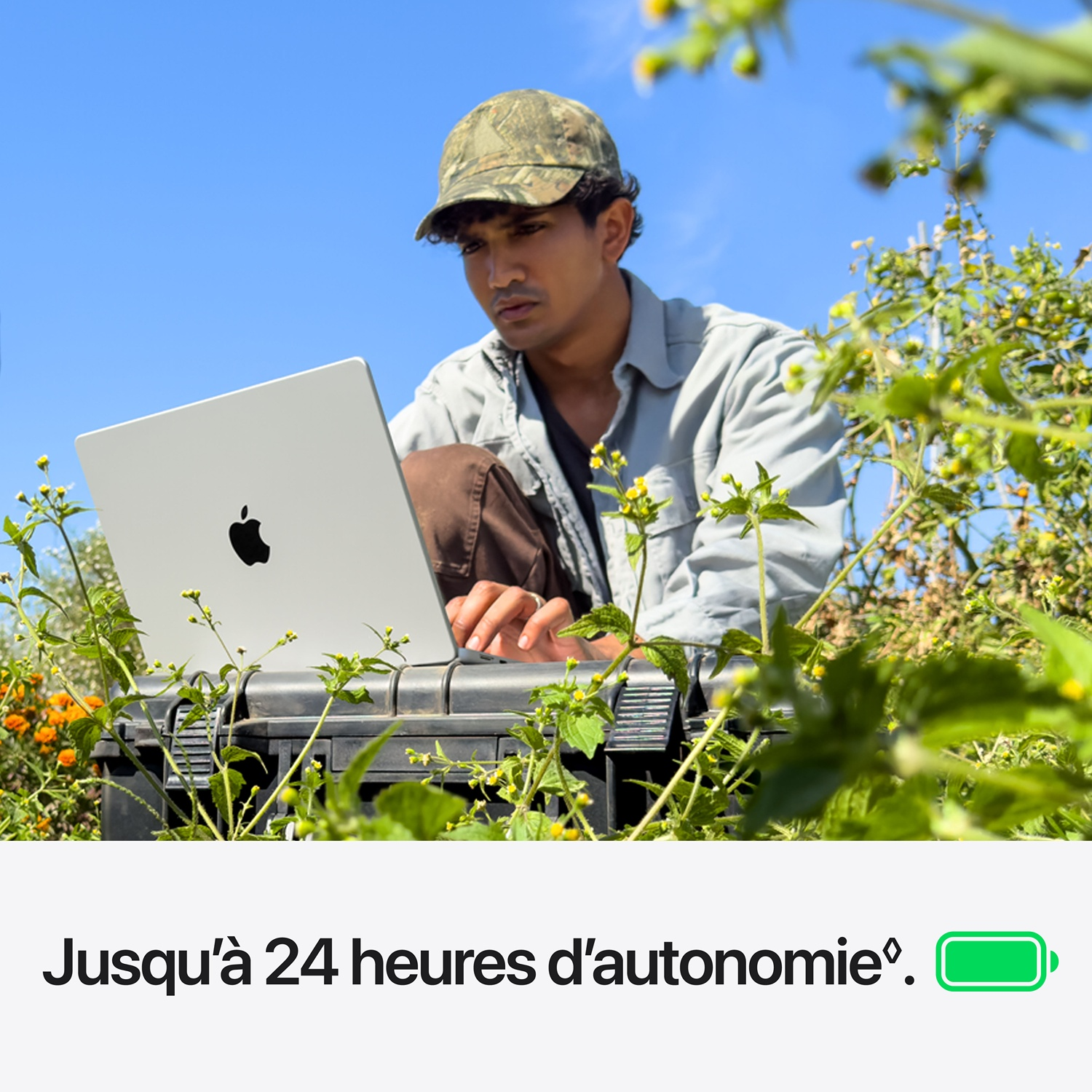 Un homme portant une casquette travaille en plein air dans un champ sur un ordinateur portable.