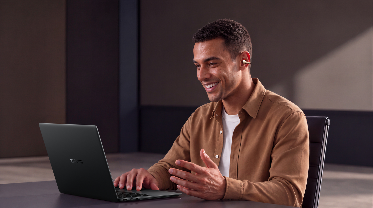 Un hombre sonriente se sienta frente a una computadora portátil con auriculares inalámbricos.
