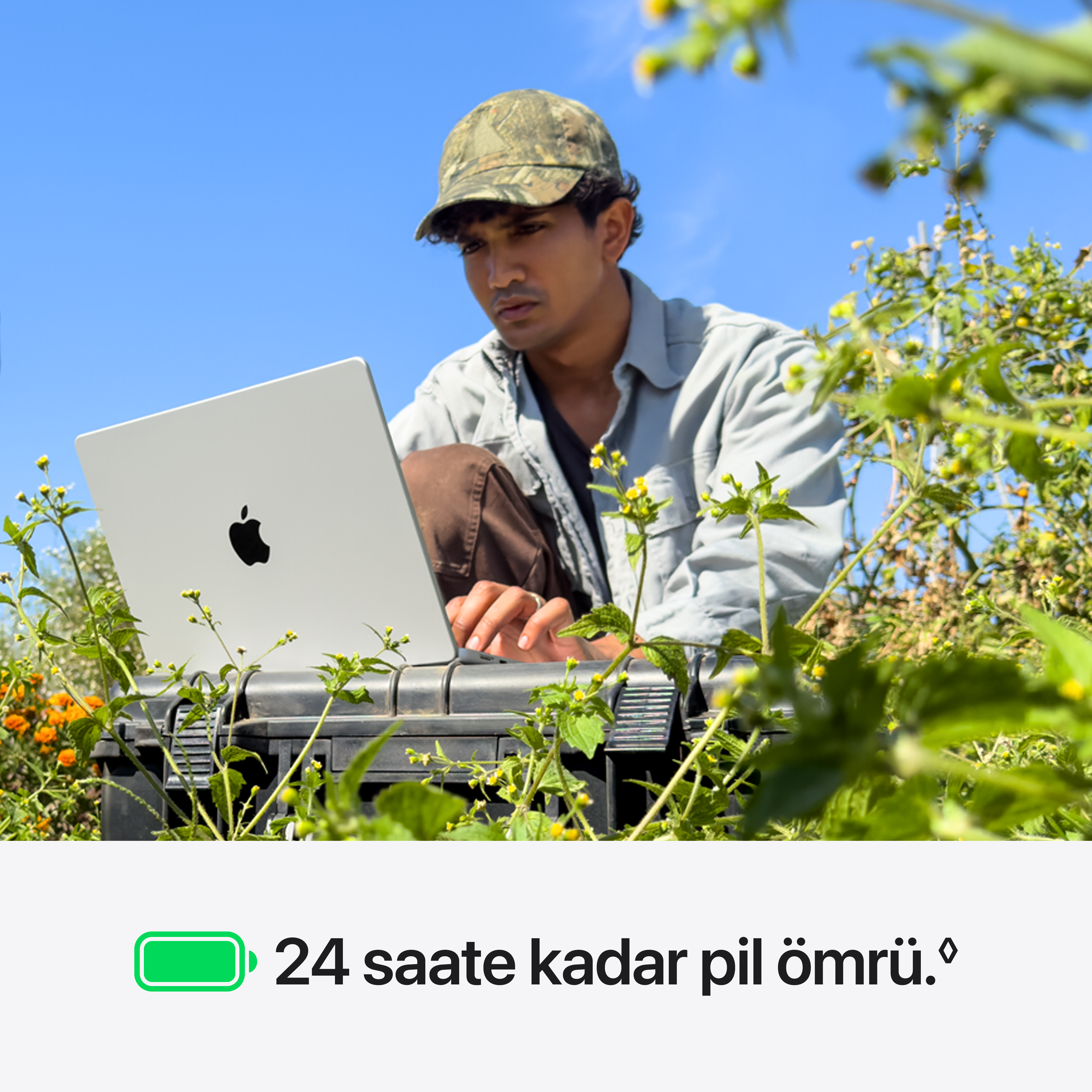 Masmavi gökyüzü altında bitkiler arasında açık havada dizüstü bilgisayar kullanan bir adam.