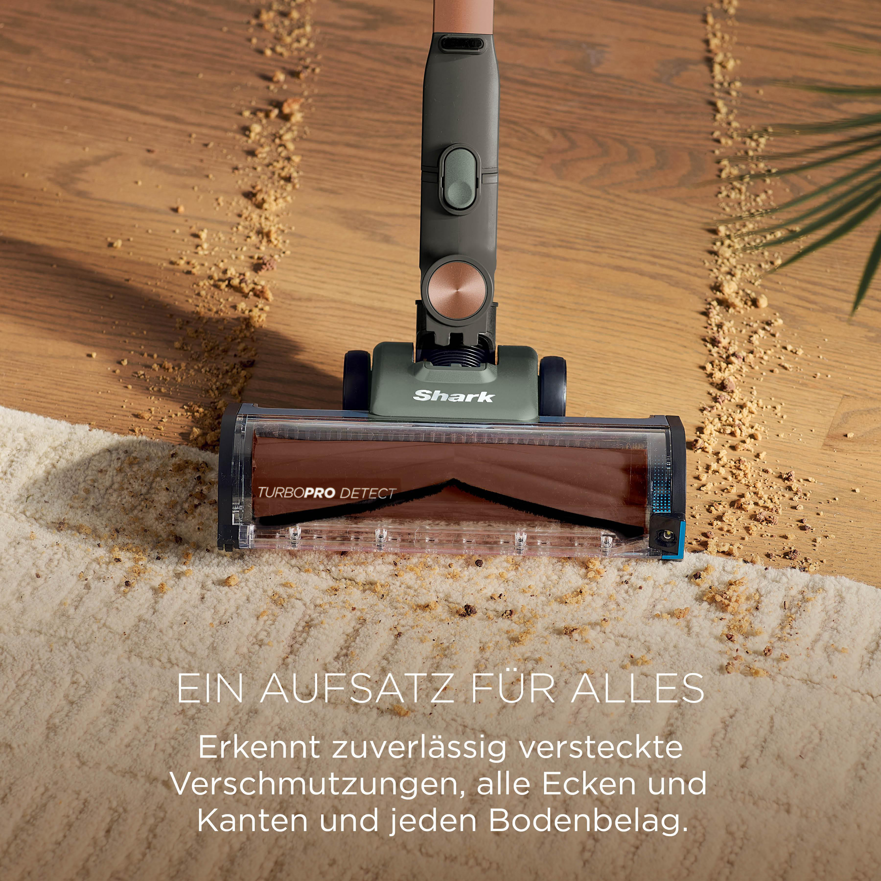 Ein Shark Staubsaugerkopf reinigt Krümel auf Holz und Teppich mit Text.