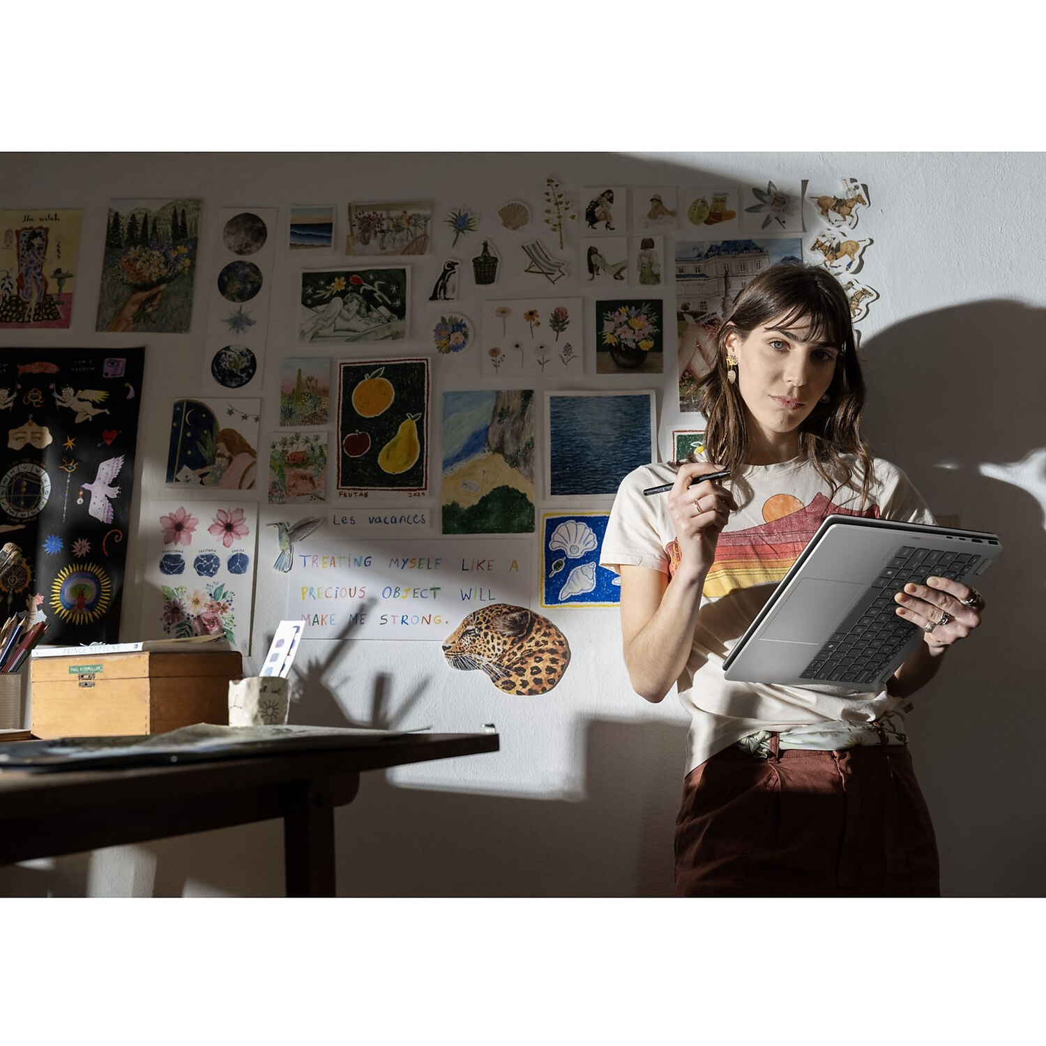Een vrouw houdt een laptop vast voor een muur vol kleurrijke kunstwerken.
