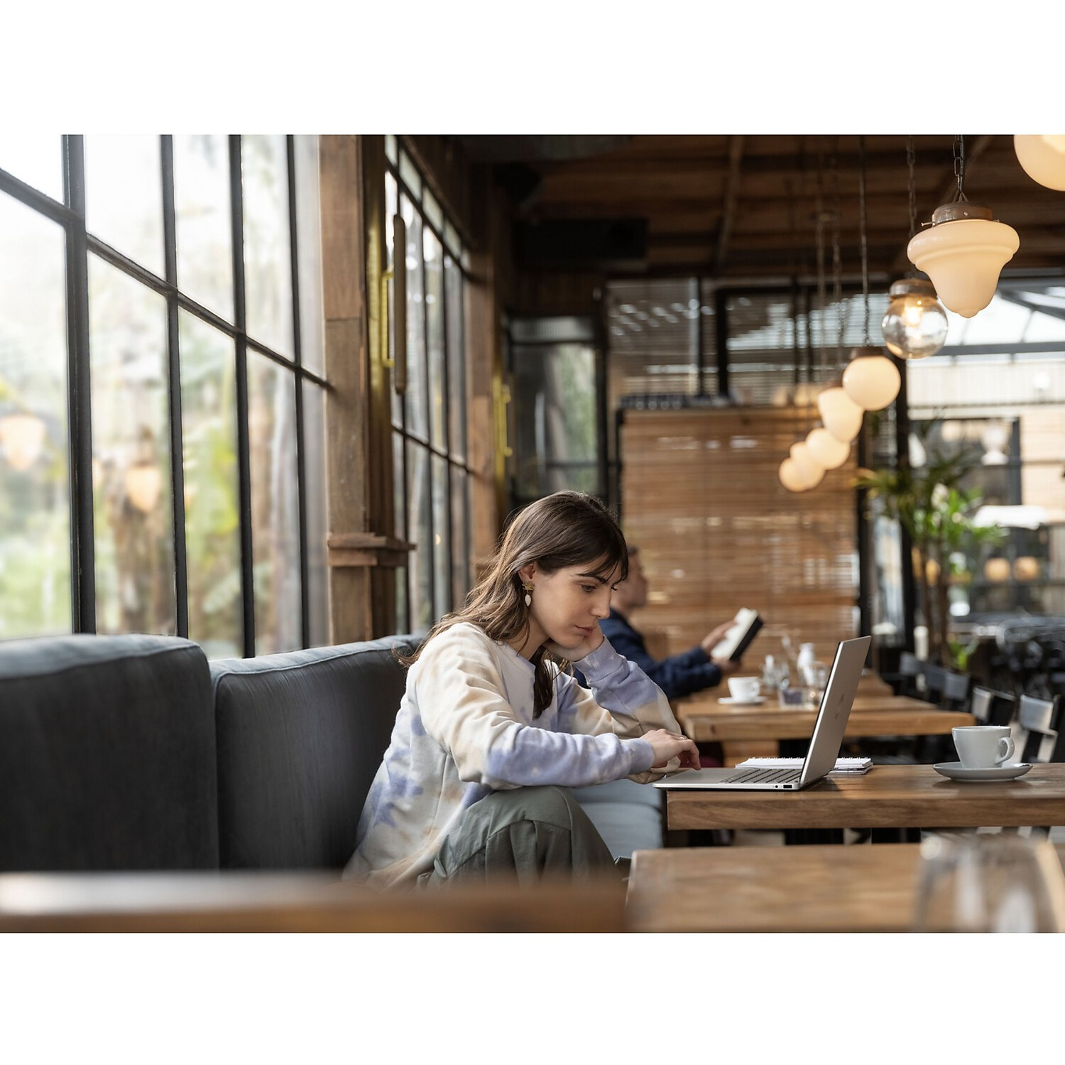Een vrouw werkt aan haar laptop aan een houten tafel in een gezellig café.