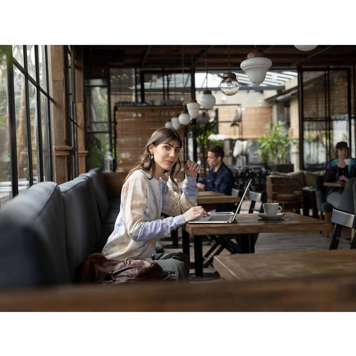 Een vrouw in een batik trui zit aan een cafatrap met een laptop.