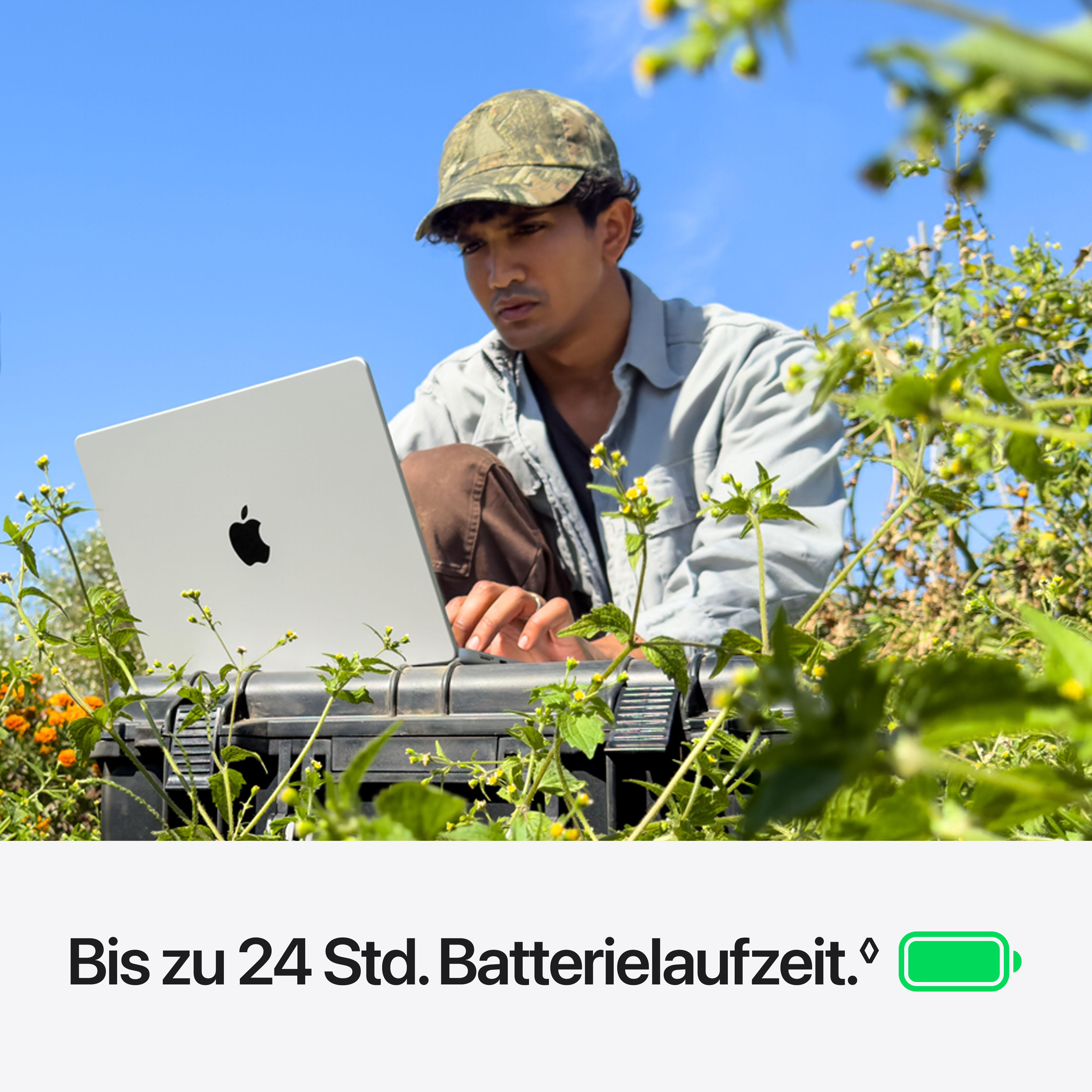 Ein Mann mit Kappe bedient im Garten einen silbernen Laptop auf einer Kiste.