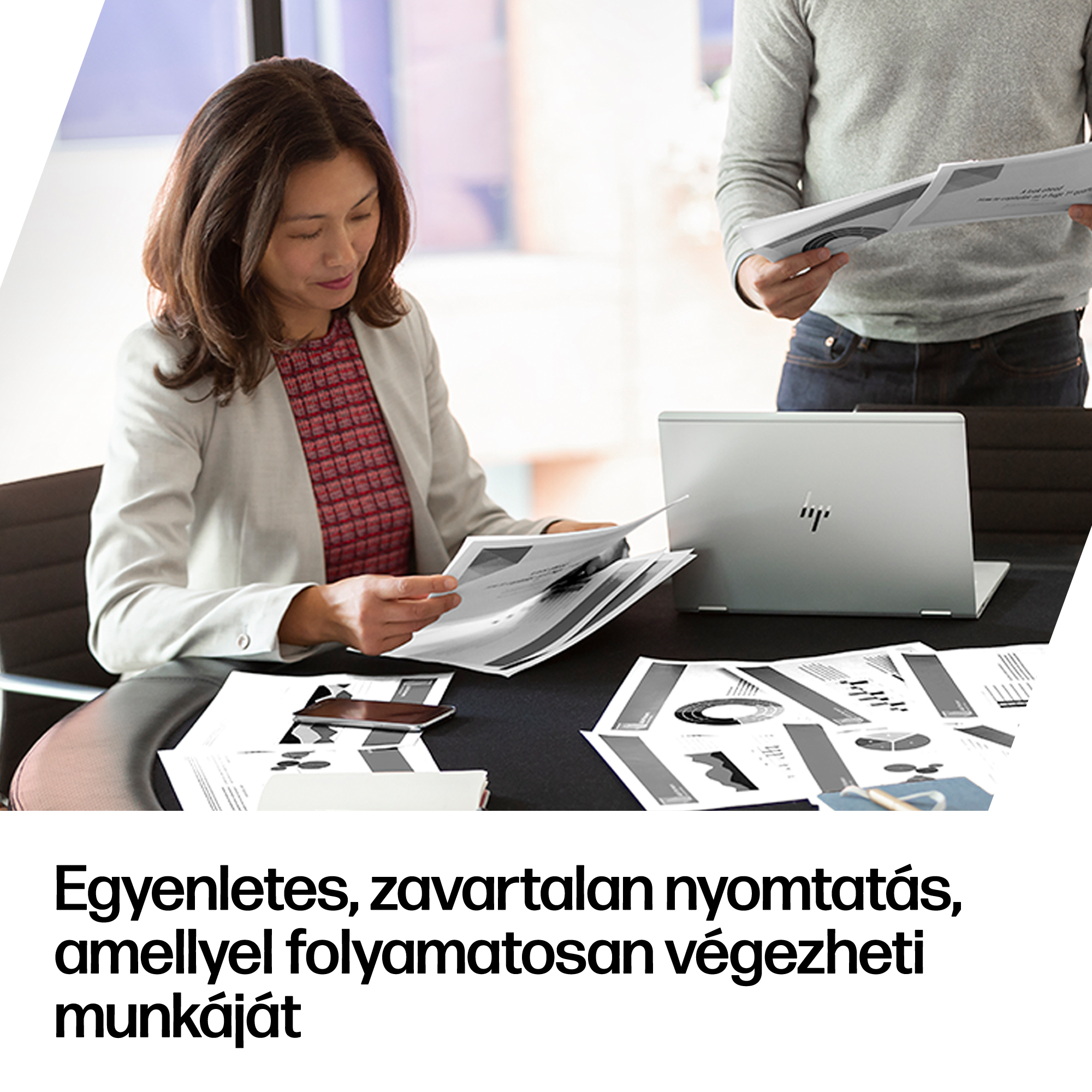 Egy nő dokumentumokat néz az asztalnál, miközben egy férfi papírokat tart a kezében.