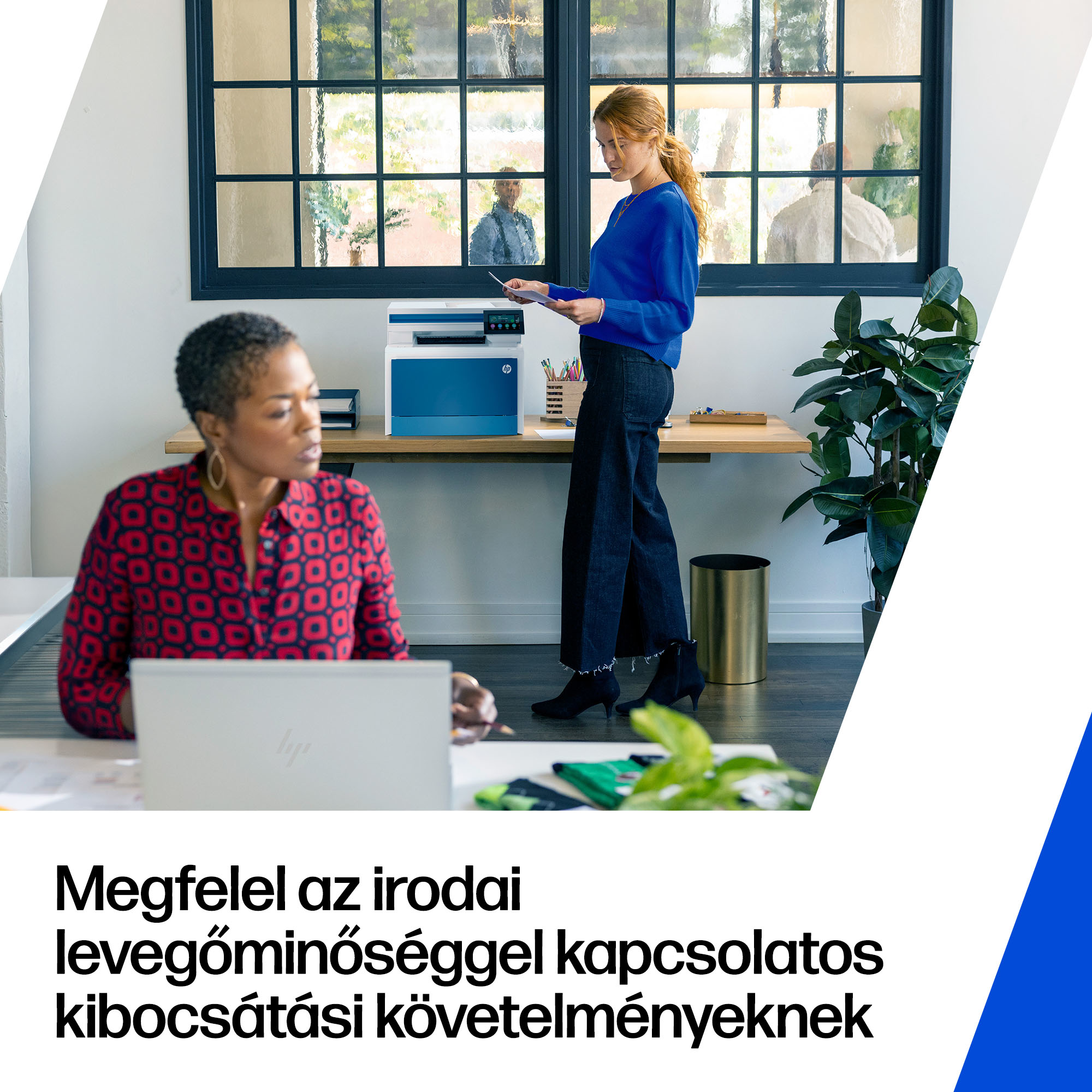 Két nő dolgozik egy modern irodában; egyikük laptopnál ül, a másik egy nyomtatónál áll.