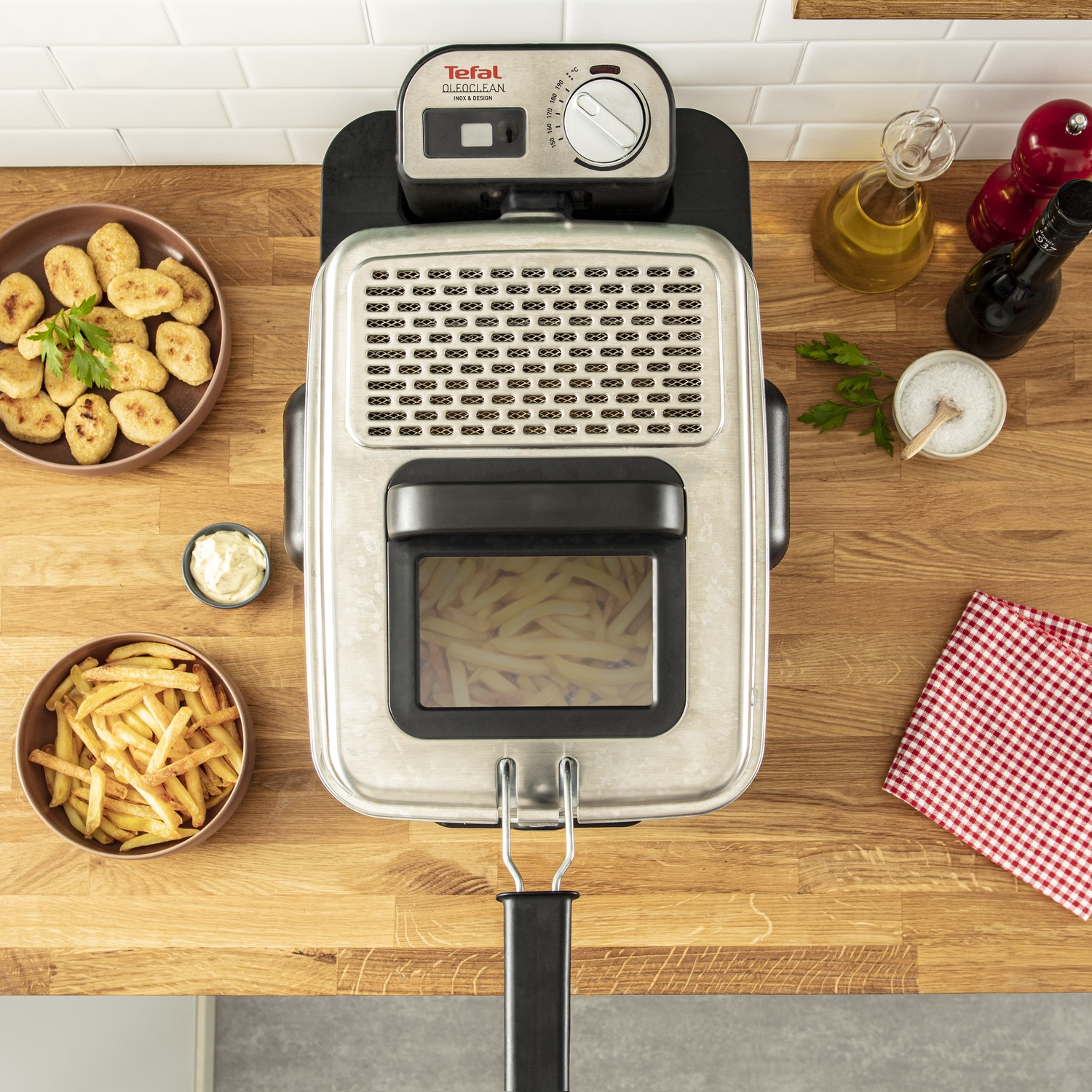 Une friteuse Tefal repose sur un comptoir en bois, entourée de frites et de condiments.