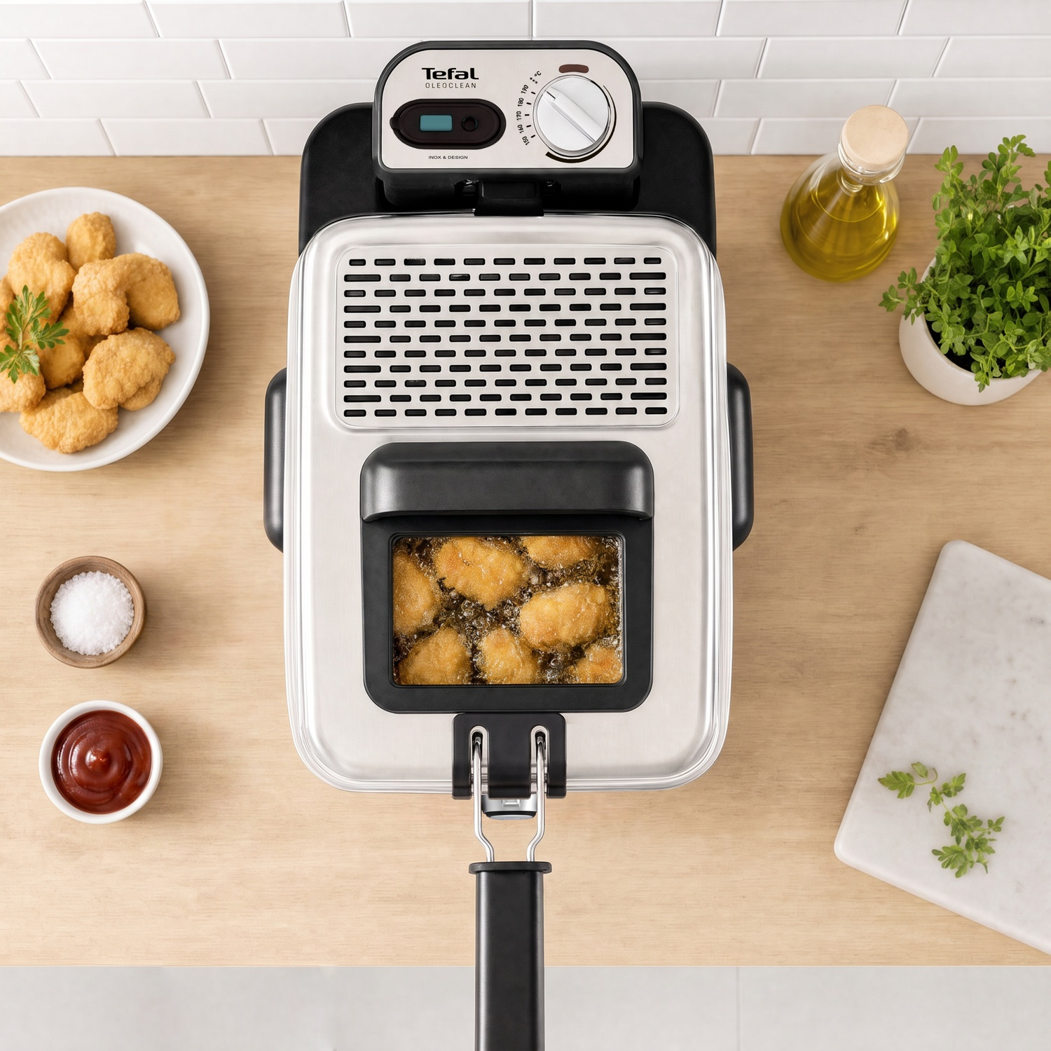 Une friteuse Tefal sur un plan de travail en bois avec des croquettes, de l'huile, du sel et des herbes.