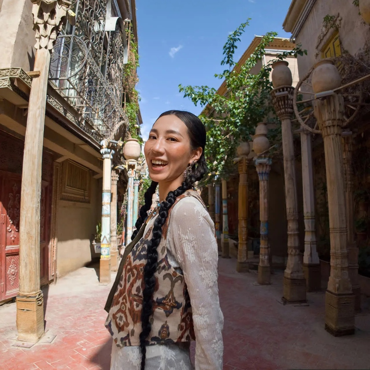 Una donna sorridente con trecce in una strada tradizionale con colonne decorate.