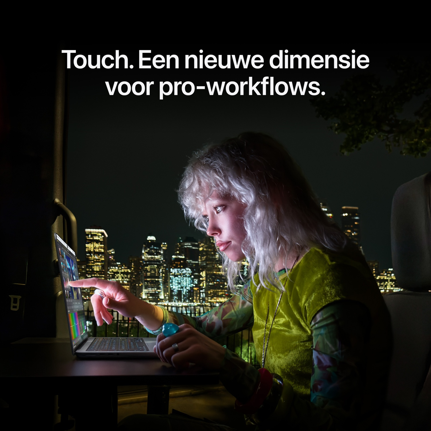 's Nachts tikt een vrouw met blond haar op een laptop tegen een achtergrond van een verlichte stad.