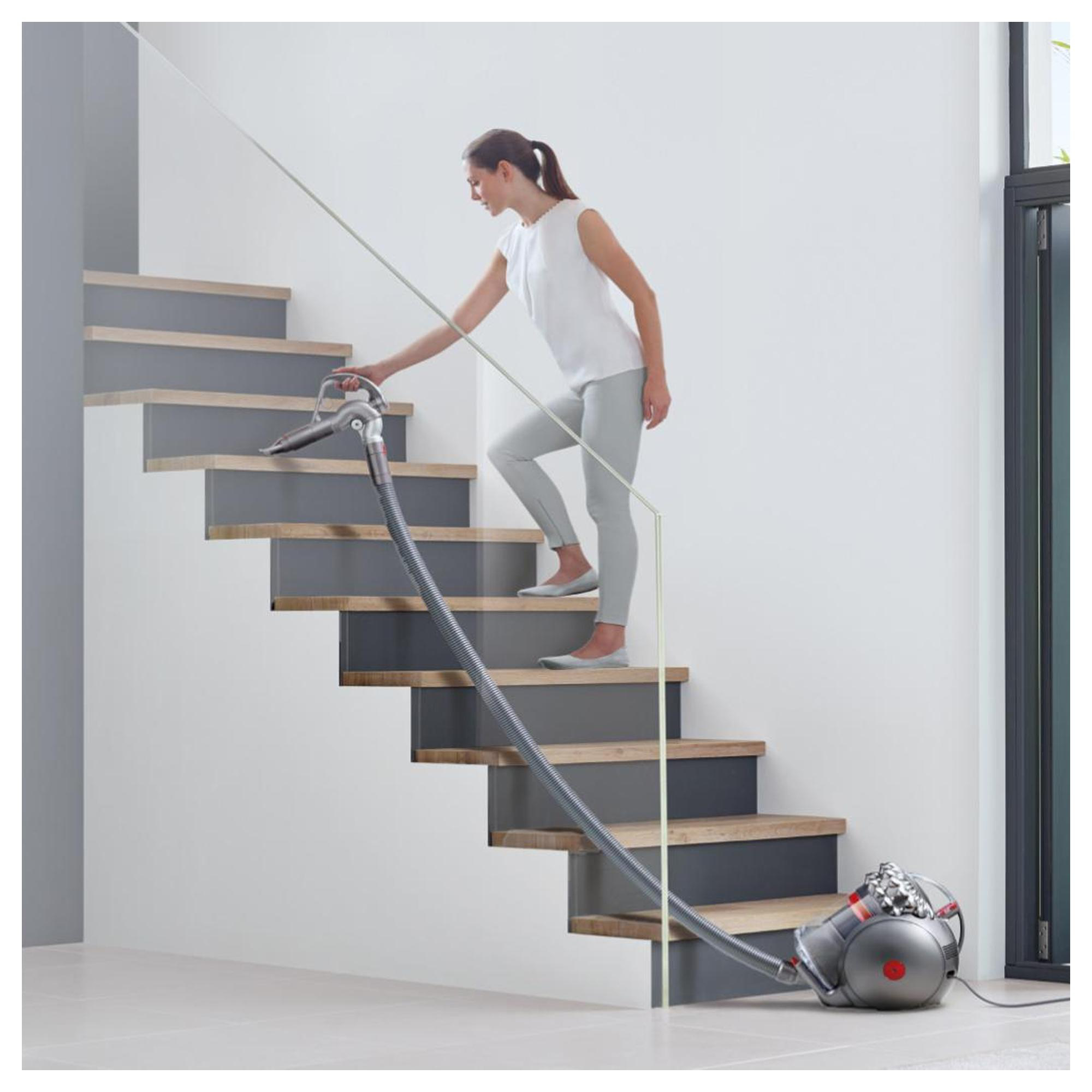 Eine Frau in weißer Bluse und grauer Hose saugt eine moderne, graue Treppe mit einem Zylindervakuum.