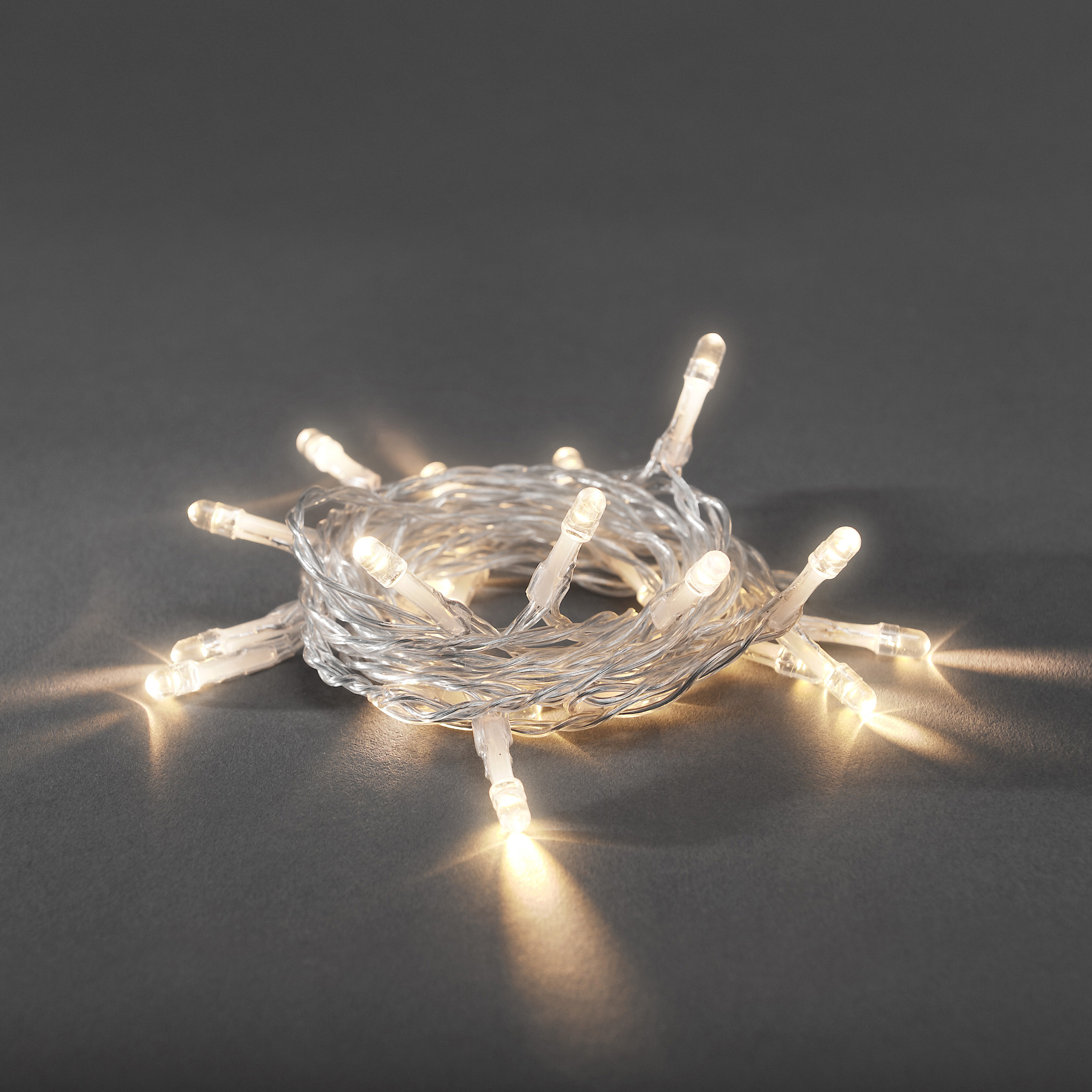Lichterkette auf einer Oberfläche aufgewickelt. Warmweiße LEDs. Grauer Hintergrund. Lichter leuchten.