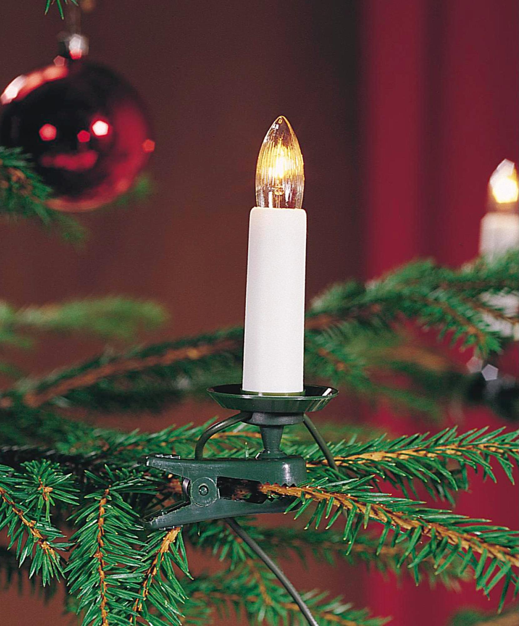 Eine weiße kerzenförmige Leuchte mit einem grünen Clip, die auf einem Weihnachtsbaum platziert ist.