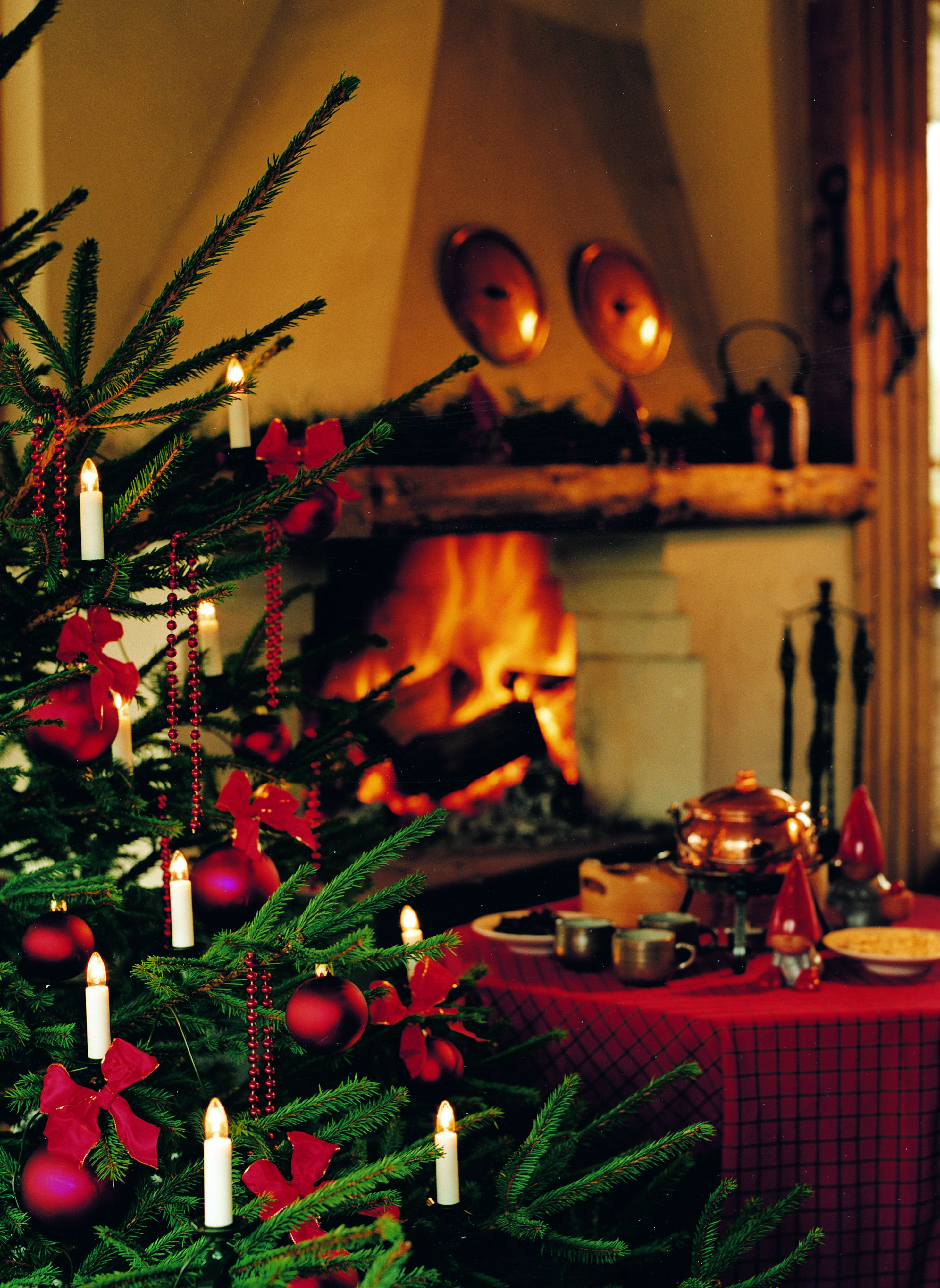 Weihnachtsbaum mit Ornamenten, Kerzen und Kamin im Hintergrund.