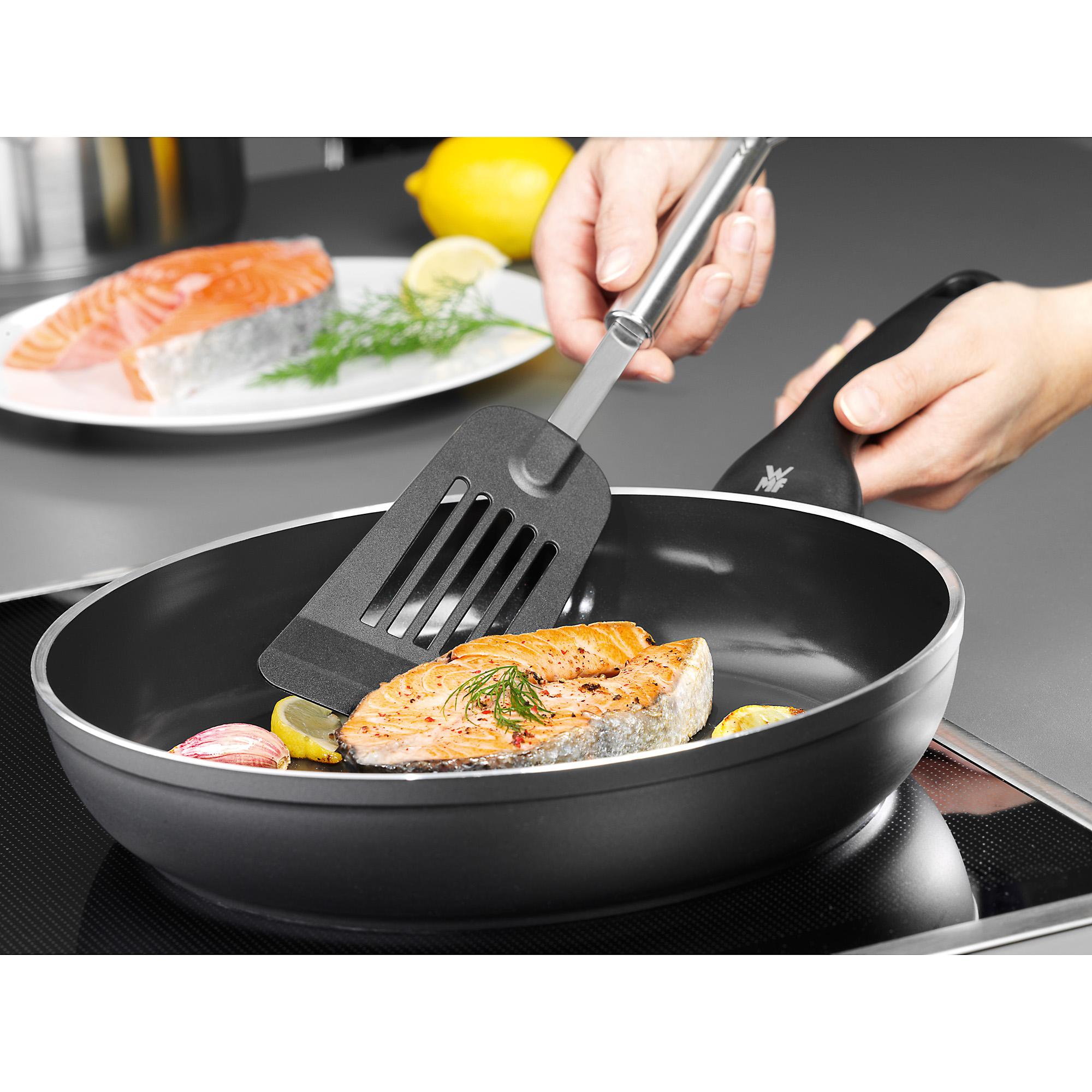 Lachs in der Pfanne mit Zitrone und Knoblauch, wird mit einem Schlitzwender gewendet.