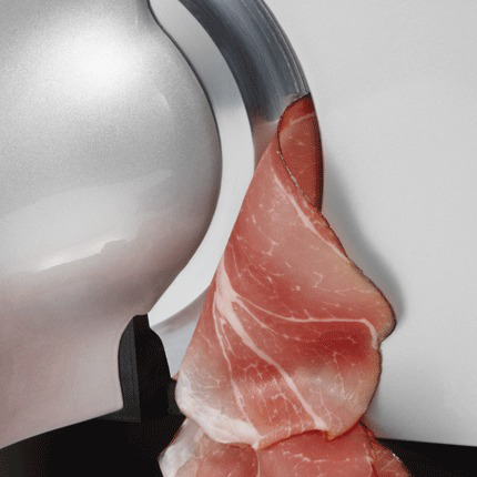 Ein Fleischschneider schneidet dünne Scheiben Prosciutto. Das Fleisch ist rosa und der Schneider ist silber und weiß.