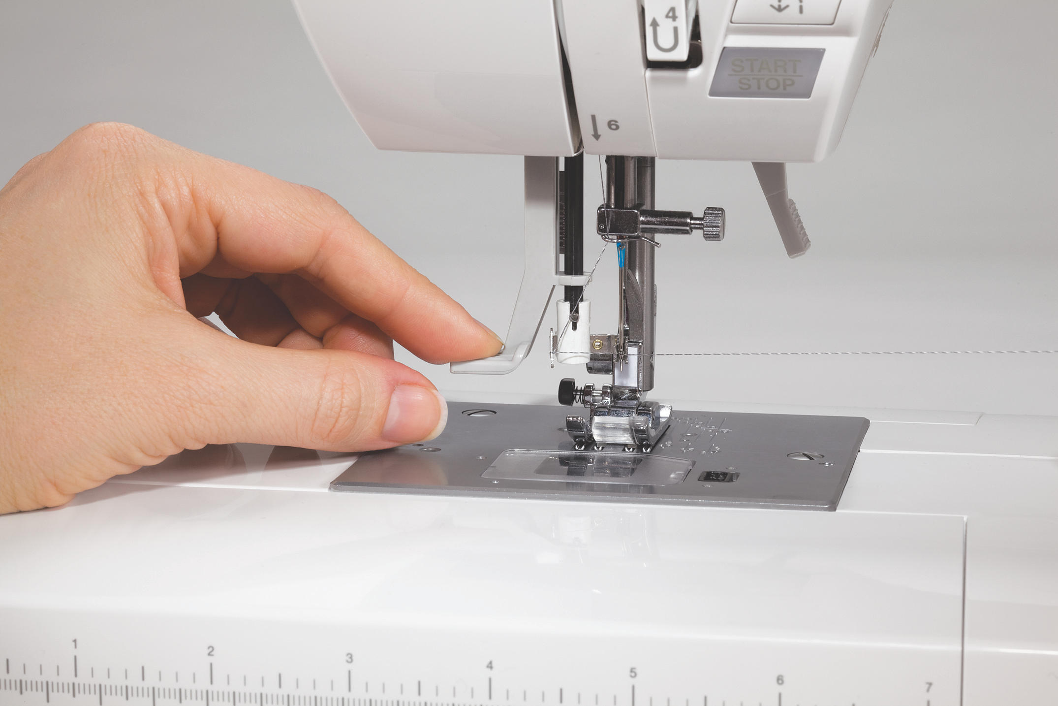 Eine Hand, die eine Nähmaschine benutzt und ein klares Plastikteil in die Nähe der Nadel legt.