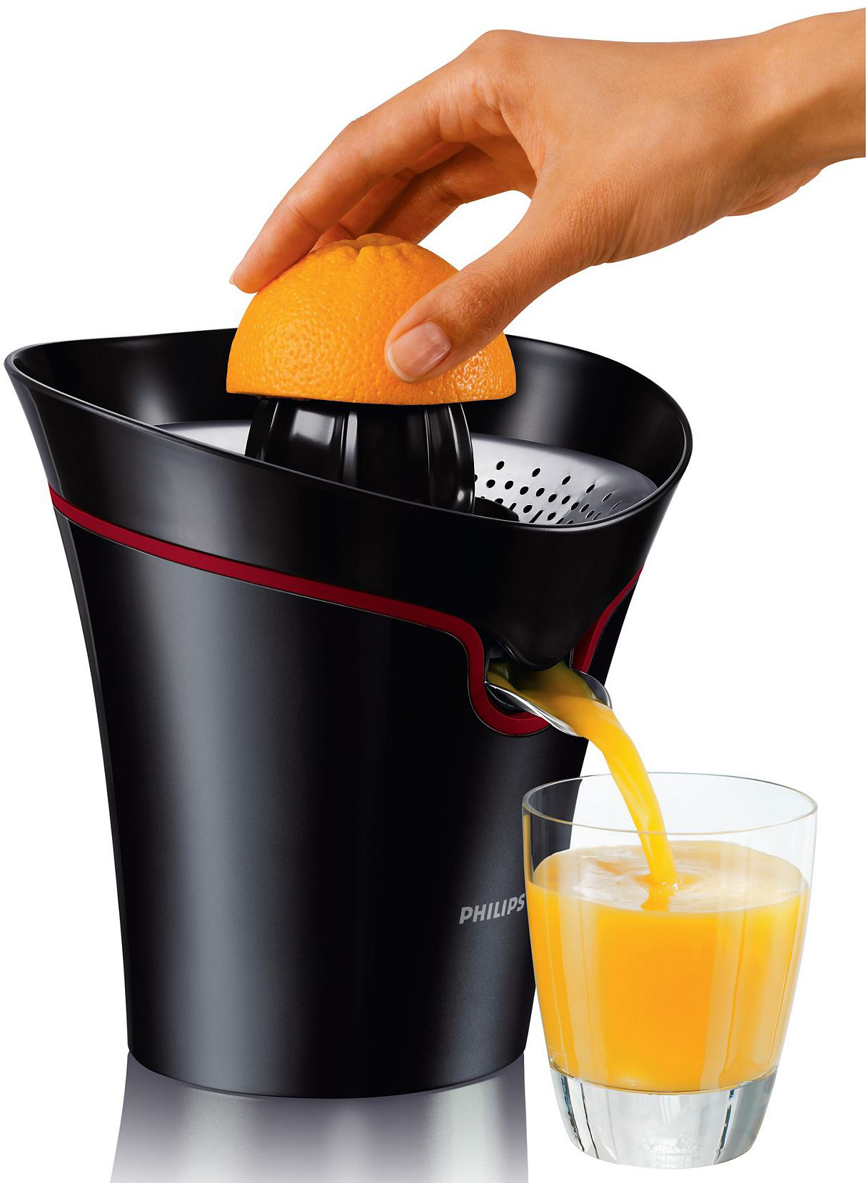 Eine Hand presst eine Orange in einen schwarz-roten Entsafter. Saft fließt ins Glas.