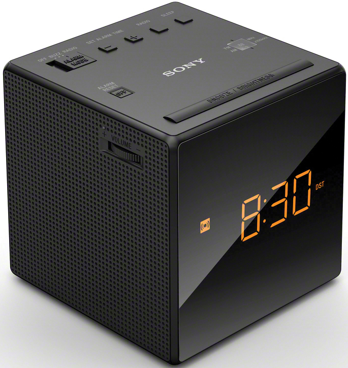 Black cube alarm clock. Digital display shows 8:30. Buttons for radio, alarm, and snooze.