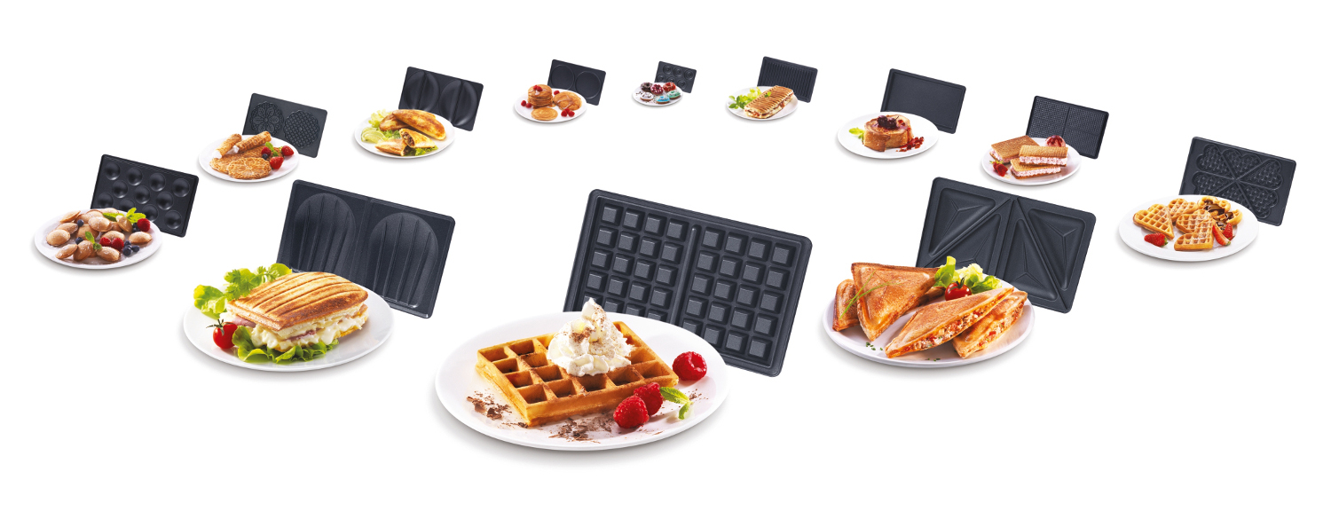 Verschiedene gekochte Speisen auf Tellern, Waffeleisen und Waffel. Alles auf weißer Fläche.