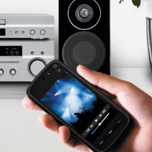 A hand holding a phone with a music player screen, speakers in the background.
