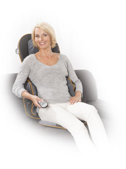 A woman sits in a massage chair, holding a remote control in her hand.