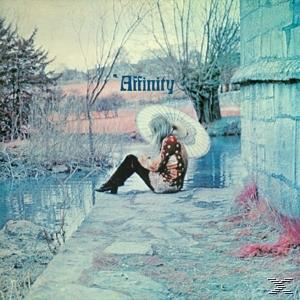 Albumcover Affinity, eine Frau mit Hut, sitzt an einem See mit Bäumen. Der Hintergrund ist blau.