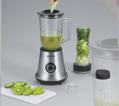 Un mixeur avec des ingrédients verts, un récipient avec des produits verts et du kiwi tranché sur une planche.
