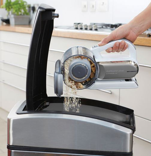 Hand holding a vacuum over a trash can, contents being emptied.