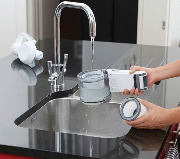 A person cleaning a vacuum filter in a kitchen sink. Water is running. Other parts are on the counter.