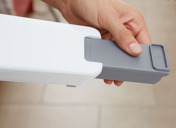 A hand is pulling a gray rectangular component out of a white box. The arrow indicates the removal direction.