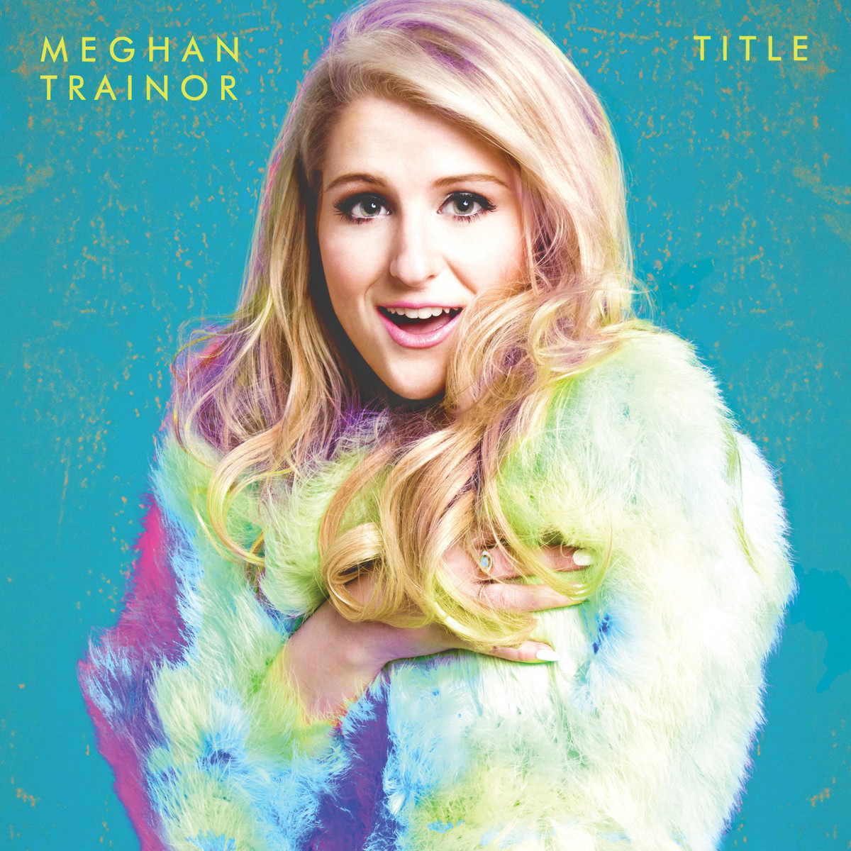 Meghan Trainor mosolyog, színes szőrmekabátot visel, kék háttérrel. A 'TITLE' szöveg látható.