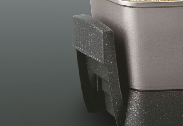 Close-up van een zwarte handgreep van een product. De handgreep is getextureerd en bevestigd aan een metalen oppervlak.