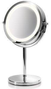 A round, illuminated mirror with a chrome stand. The mirror reflects light, and the stand is on a circular base.