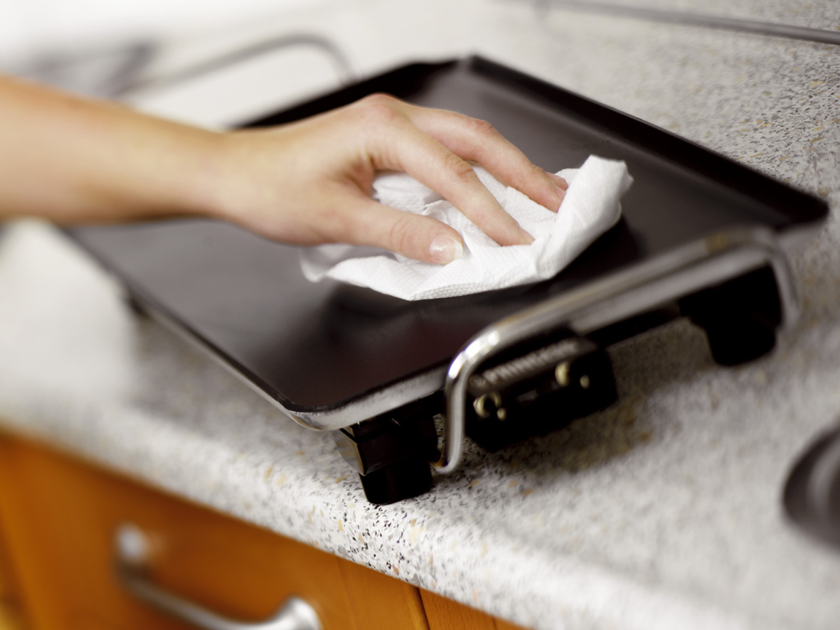 A hand wiping a black griddle with a white paper towel.