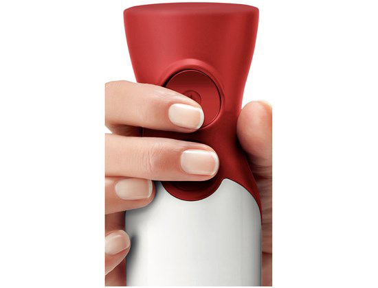 Een hand drukt op een knop van een rode en witte staafmixer, close-up.