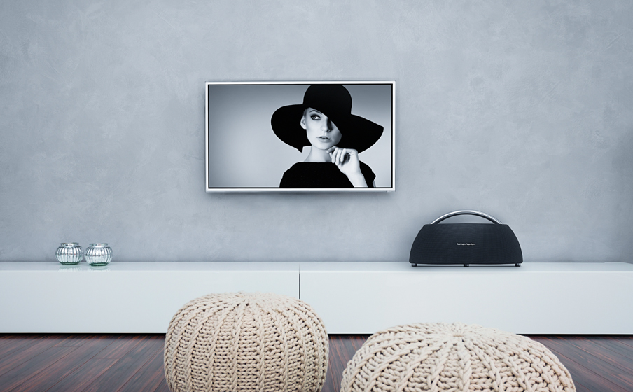 Een moderne woonkamer met een vrouw met een hoed op een tv-scherm en een luidspreker op de plank.