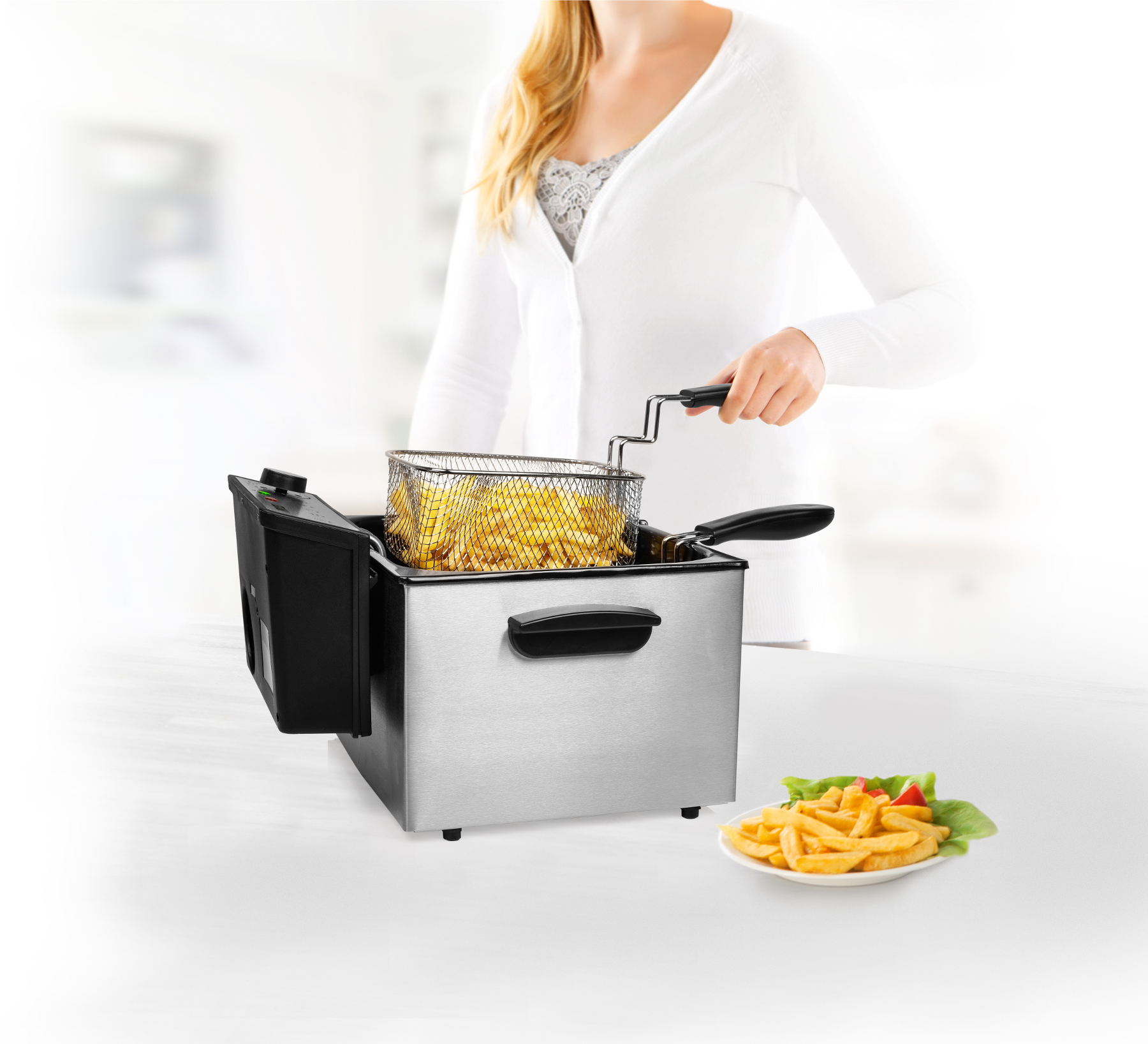 Een vrouw bakt friet in een roestvrijstalen friteuse. Friet op een bord.