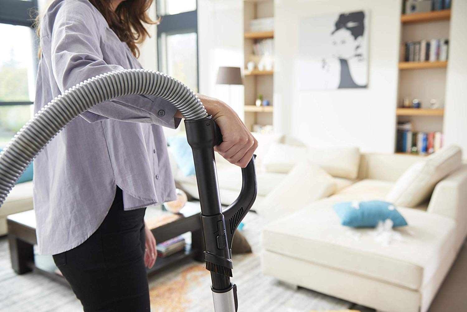 Una mujer aspira una habitación. Sofá y estanterías al fondo.
